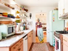 Woman with blue hair in doorway of pastel kitchen. 