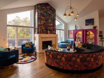 Large room w/ graffiti fireplace, round sofa + chairs, + bright rugs.