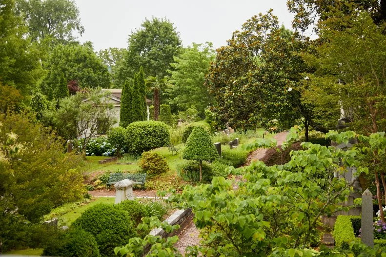 Lush green park dotted with trees, grave stones and brick paths