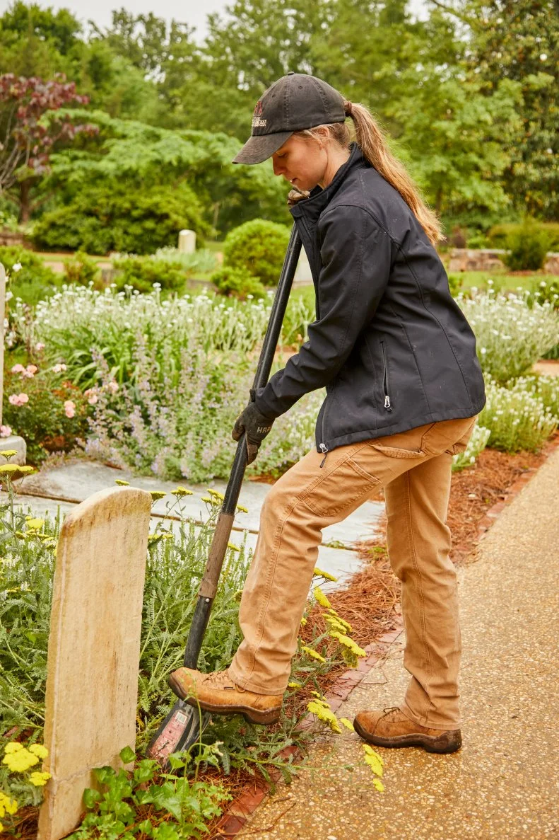 A person with a shovel landscapes around a tombstone.