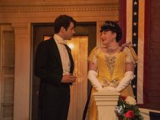 Man in tux and tails speaking with woman in yellow Victorian dress. 