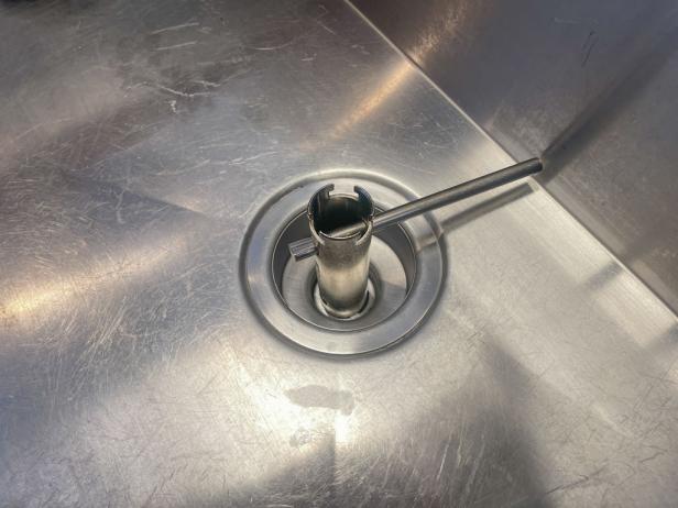 The next step in installing a garbage disposal is to remove the drain flange using a basket strainer wrench.