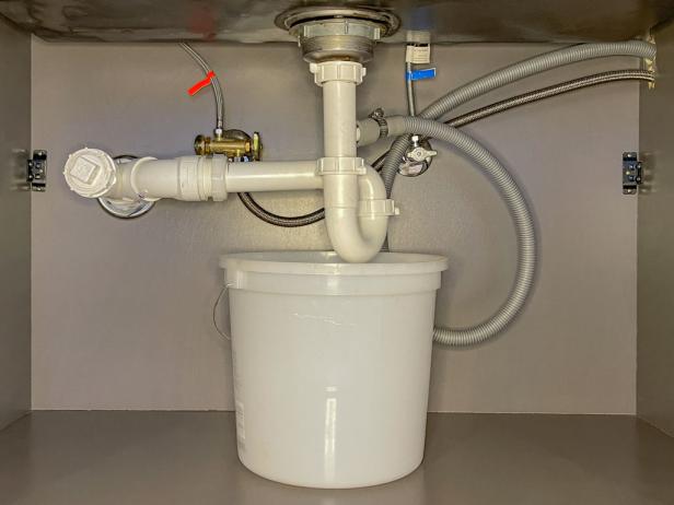 The next step in installing a garbage disposal is to place a bucket beneath the P-trap to catch the water as you unscrew it.