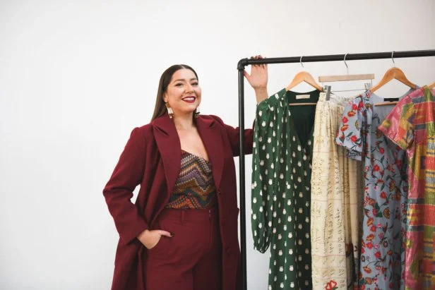 Woman Standing, Smiling With Rack of Dresses