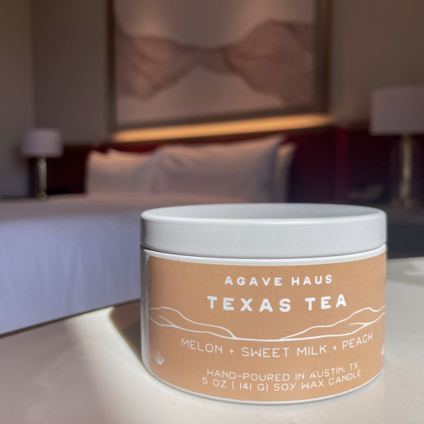 A candle win with a tan label on a bedroom table.