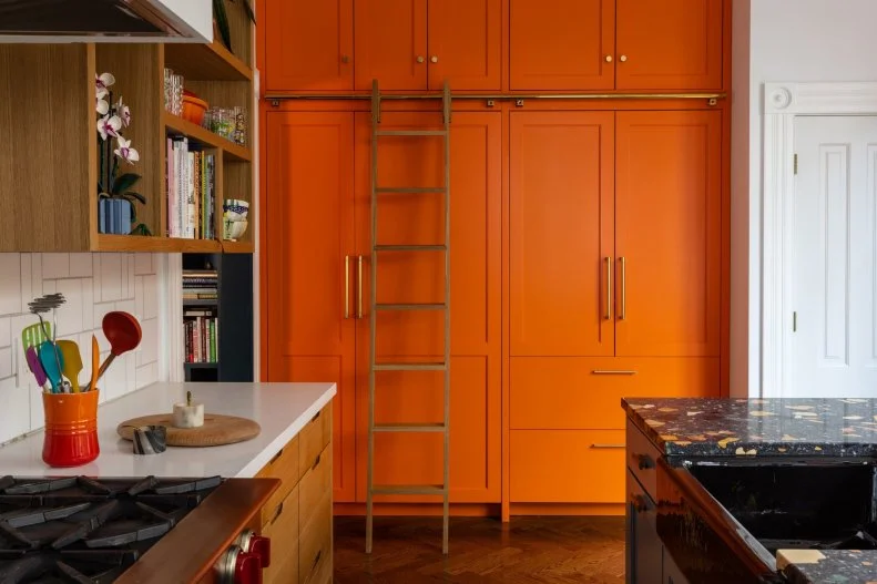 An orange pantry with gold hardware in a kitchen with high ceilings. 