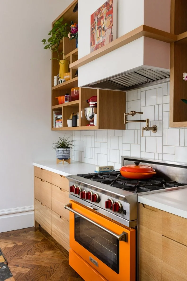 Orange gas range in a kitchen with light brown cabinets and white wall