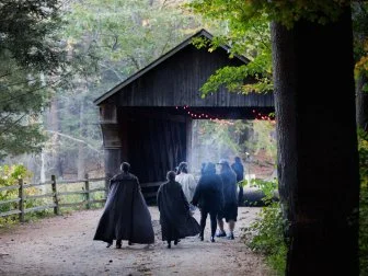 Visitors in Halloween costumes cross over a covered bridge in Old Sturbridge Village as twilight approaches.