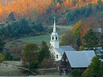 An aerial view of a small church surrounded by trees in fall foliage at sunrise in Corinth