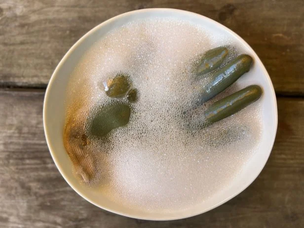 Dirty rubber gardening gloves in a bowl of soapy water.