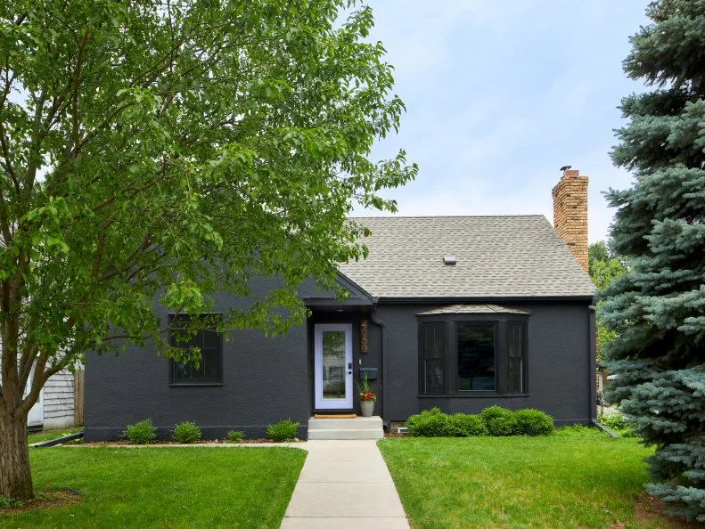 Black Stucco Bungalow With a Light Purple Front Door