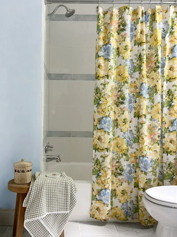 HGTV Magazine presents this bathroom makeover with marble-look tiles, blue walls and a floral shower curtain.