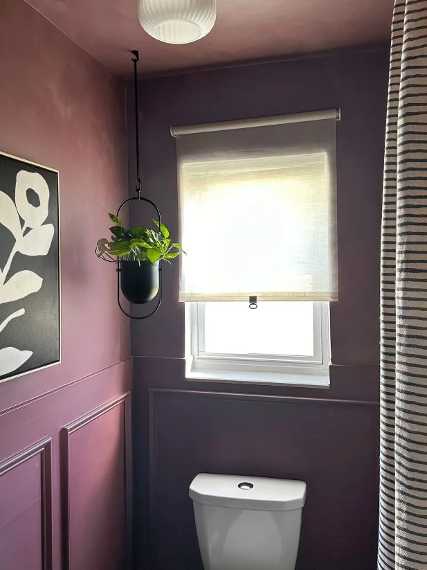 HGTV Magazine shares the details of this deep, brown-ish purple painted bathroom with decorative trim, a striped shower curtain and a hanging planter.