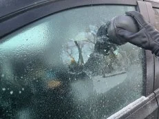 Using an electric ice scraper to get rid of ice on a vehicle window.