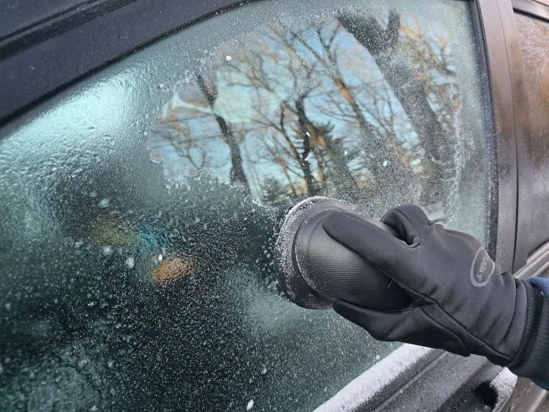 Using an electric ice scraper to get rid of ice on a vehicle windshield.