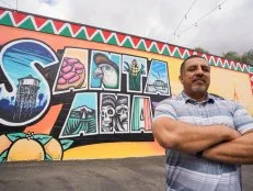 Izzy Battres poses in front of a Santa Ana mural as seen on the Izzy Does it pilot.