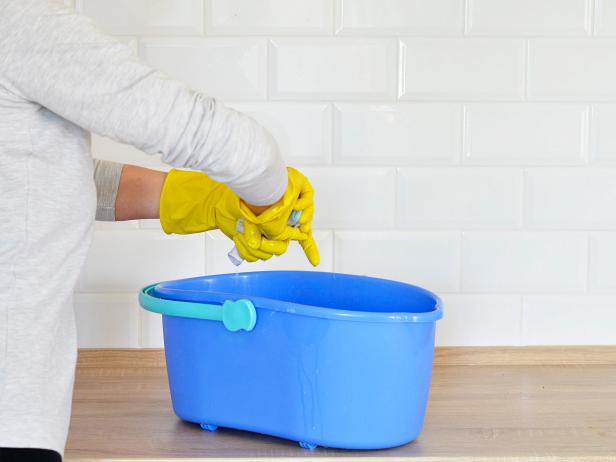 woman washes white tiles on a wooden board has a blue bucket