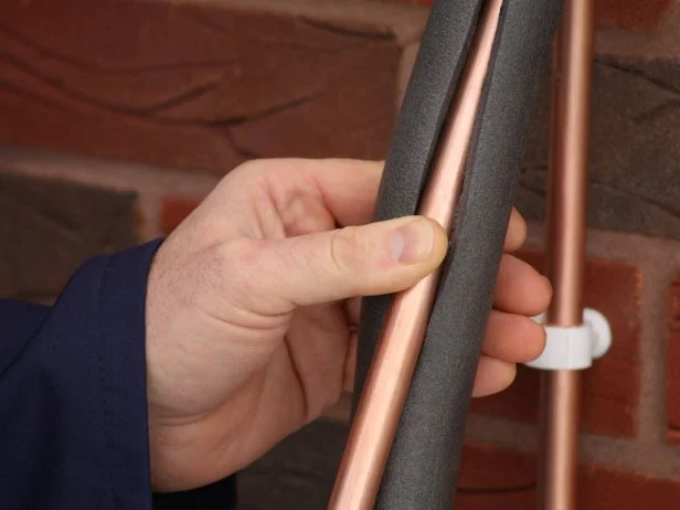 "Plumber applying insulation to copper water pipes,focus on insulation."