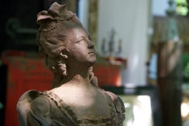 A cast iron bust of a Marie Antoinette in dappled sunlight. 