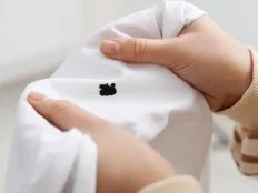 Woman holding white shirt with black ink stain on blurred background, closeup