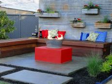 Corrugated metal is used to  build a privacy wall and create a backdrop for a fun gathering space. To  make the unusual fire pit, a gas line was run through the recycled  metal bucket then filled with lava rock.