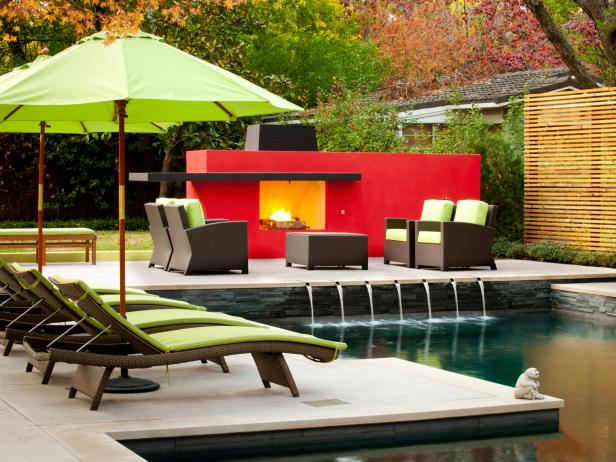 This outdoor patio next to the swimming pool contains a bold red fireplace with sleek lines.