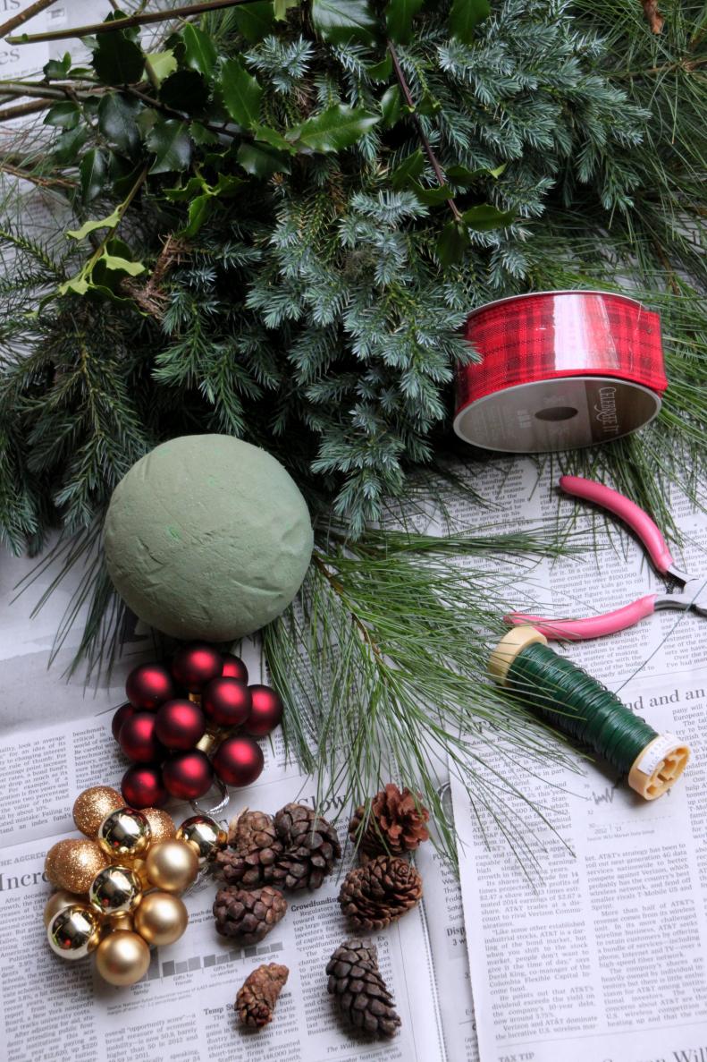 You will need: Assorted greenery/Garden clippers/4 inch round foam floral ball/24 gauge floral wire/Ribbon/Scissors/Wired glass balls/PInecones/Wire cutters/Newspaper.