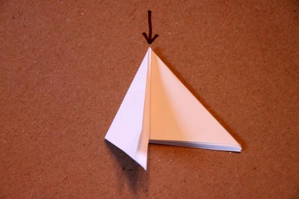 Fold the paper in half at the arrow but pull the tip of the triangle down like so.