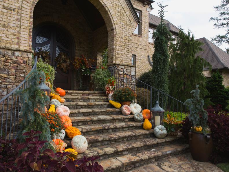 Brightly colored fall vegetables create a dramatic, inviting entrance to Brenda Addington's home in Suwanee, Georgia. Set against the porch's rough-textured stone facade and steps, the seasonal color pops. The display includes mums, pumpkins, gourds and squashes. At night, candlelight from large-scale lanterns adds to the autumn ambiance.