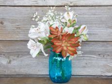 Stunning red succulent stands out among white genista and white alstroemeria in a Mason jar arrangement by <a target="_blank" href="https://www.thebouqs.com/en/64-all?bcid=1235&amp;utm_medium=partnerships&amp;utm_source=hgtv&amp;utm_campaign=hg...">The Bouqs</a>.