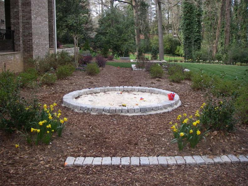 A section of yard can be carved out for a mulched bed and special feature, such as a sandbox with simple stone elements.