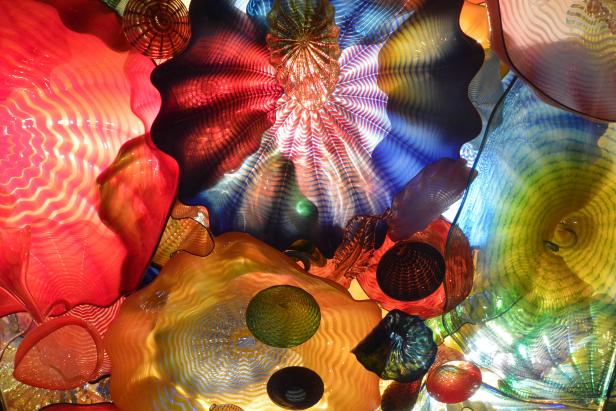 Visitors walk beneath glass floral shapes lit from behind in the Persian Ceiling. This lighting casts colored shadows on the walls and floors. Chihuly calls these forms &quot;the Persians.&quot; He began this glass art series in 1986. The first Persian Ceiling was presented in his 1992 exhibition at the opening of the downtown Seattle Art Museum.