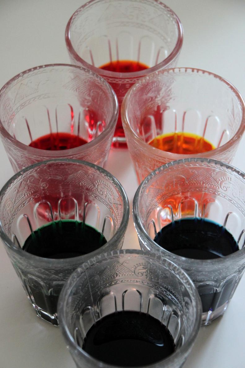 In the bottom of each cup, add a few drops of food coloring. The more you add the darker the tint on the flowers. A good ratio is 20 drops to 1 cup of water. To make purple combine 10 drops of blue and 10 drops of red. To make orange combine 10 drops of red and 10 drops of yellow.