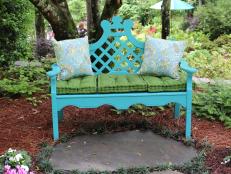 Embrace color in the garden with a bench in a striking color accented by pillows and well-placed pavers that welcome visitors to take a moment to rest and take in the view.