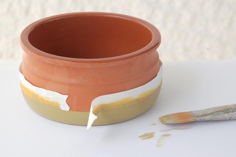 Step one is painting your pots. To create clean and even stripes, use tape to cover the parts of the pot you don't want to get paint on. Press the tape firmly against the pot, making sure there are no folds or other places paint might leak through. Paint a solid color wherever you want a stripe to be. You can use a single color, or create multiple stripes in different colors. When the paint is completely dry, peel off the tape.