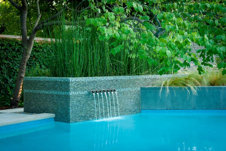 A clean, modern aesthetic informs this remodeled water feature by Pool Environments which added a fountain and raised wall to the existing pool including a veneer of glass mosaic tile and custom stainless steel scupper waterfalls.