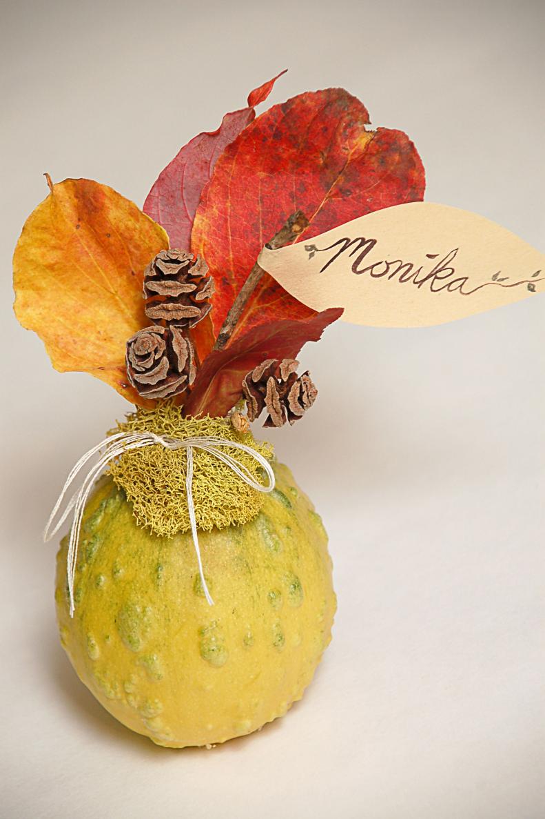 Add leaves, dried flowers, little pine cones, acorns, and whatever else you would like around your name flag, taping them onto the gourd stem as you go. When you're happy with your arrangement, wrap the base in moss to cover the tape. Tie the moss on with string or twine for a decorative finish.