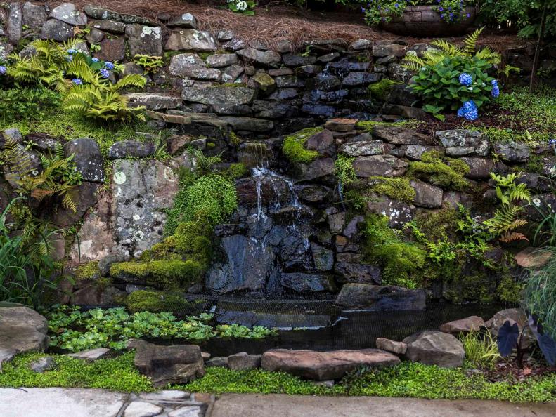 A waterfall trickles down a rock wall alongside the driveway, spilling into a water garden stocked with large Japanese koi.