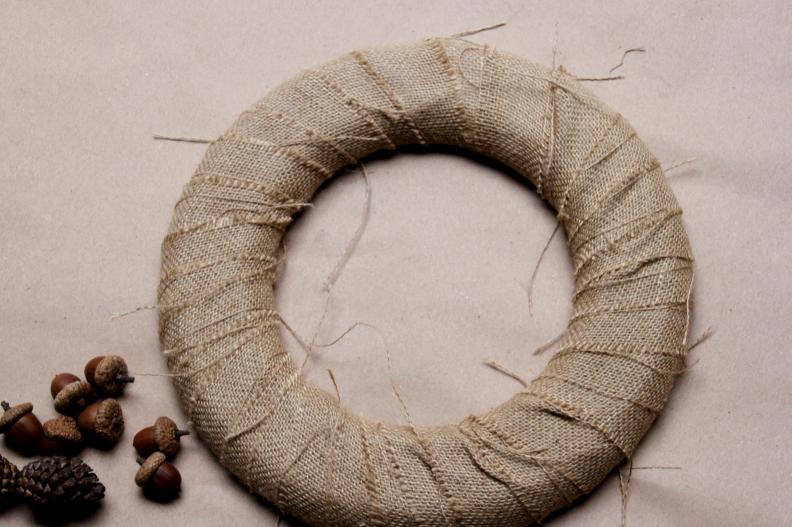 Once you have gone all the way around the wreath, glue the end of the burlap in place and cut off the excess.&nbsp;This will help the pine cones and acorns adhere to the wreath best.