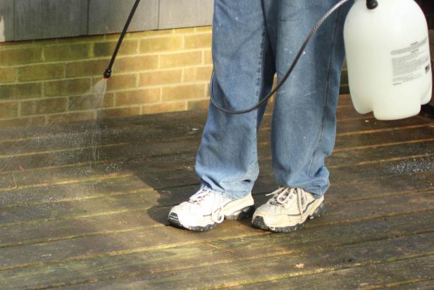 Deck cleaner can be spread by using a brush or broom to sweep across the  surface or applied using an inexpensive tank sprayer as shown here.  Make sure all edges, corners and gaps are treated as will as the deck  surface. Follow manufacturer instructions regarding use, but in most  cases, the solution should be left to soak on the wood for a period of  time before continuing.