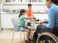 Mother in wheelchair playing chess with children (7-9) in kitchen