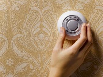 Woman adjusting thermostat on beige wallpapered wall, close-up