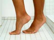 Image of person's feet standing on tiptoes on tile floor in bathroom, close-up