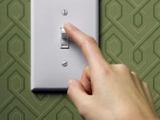 Woman turning off light switch on green wallpapered wall, close-up