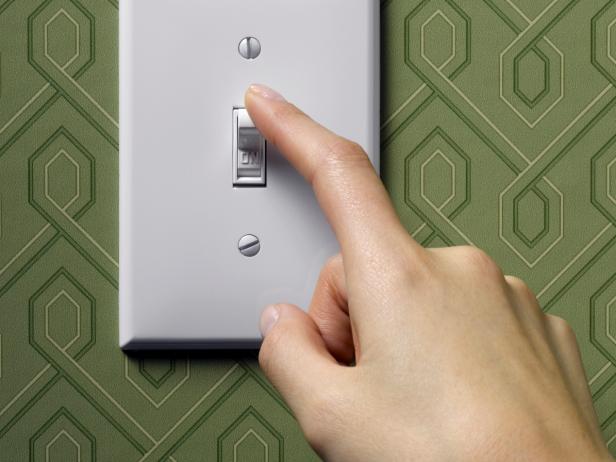 Woman turning off light switch on green wallpapered wall, close-up