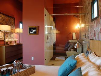 Wide view of bedroom with warm color scheme - bathroom with glass wall separating the bedroom area. 