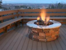Brick fire pit surrounded by wood railing and bench seating at dusk. 