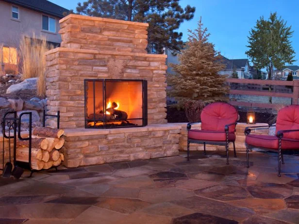 Outdoor living space with a stone woodburning fireplace, chairs, and wood storage area. 