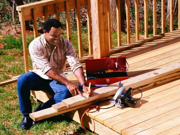 Hired deck builder measuring wood for installing a deck in this backyard space. 