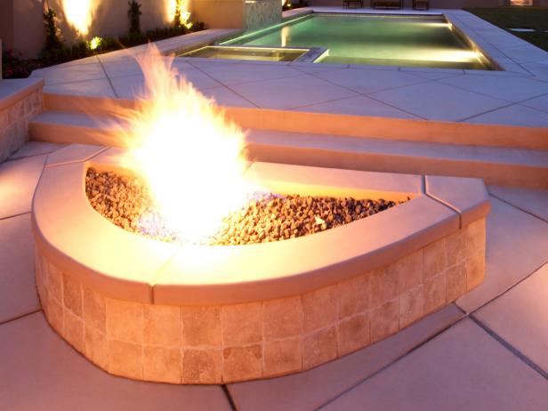 Luxury backyard with a pool and natural gas fire pit with burning flame in the foreground. 